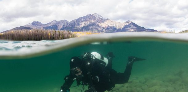 Joey Hanging Out Underwater In A Clear Alpine Lake In The Canadian Rockies With The Mountains In The Background And The Waterline Crisp, Alberta Scuba