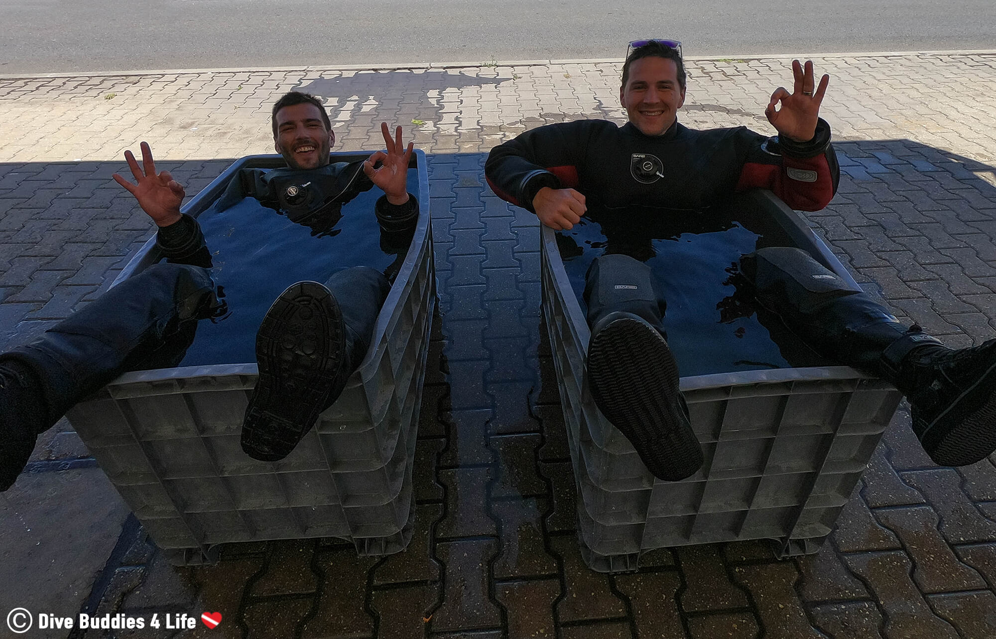 Two Divers Sitting In A Rinse Bin Cleaning Off Their Dive Equipment After A Scuba Dive In Sesimbra, Portugal, Europe